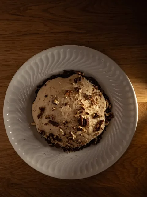 Dessert crémeux parsemé d'éclats, dans une assiette blanche cannelée posée sur une table en bois