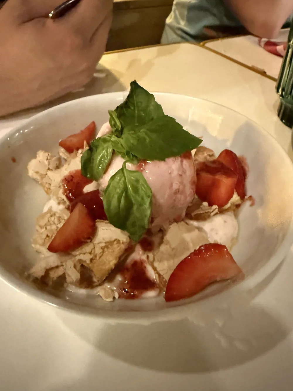 Dessert de meringue, glace rose, fraises et feuilles de basilic dans une assiette creuse