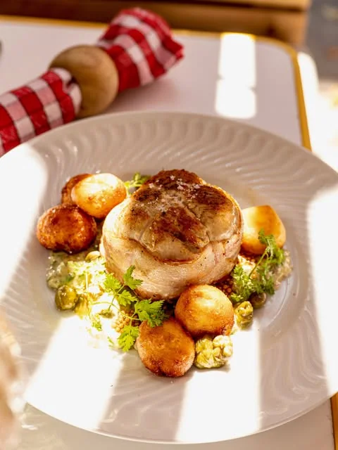 Médaillon de viande rôtie entouré de pommes de terre dorées et d'herbes, sur une assiette blanche