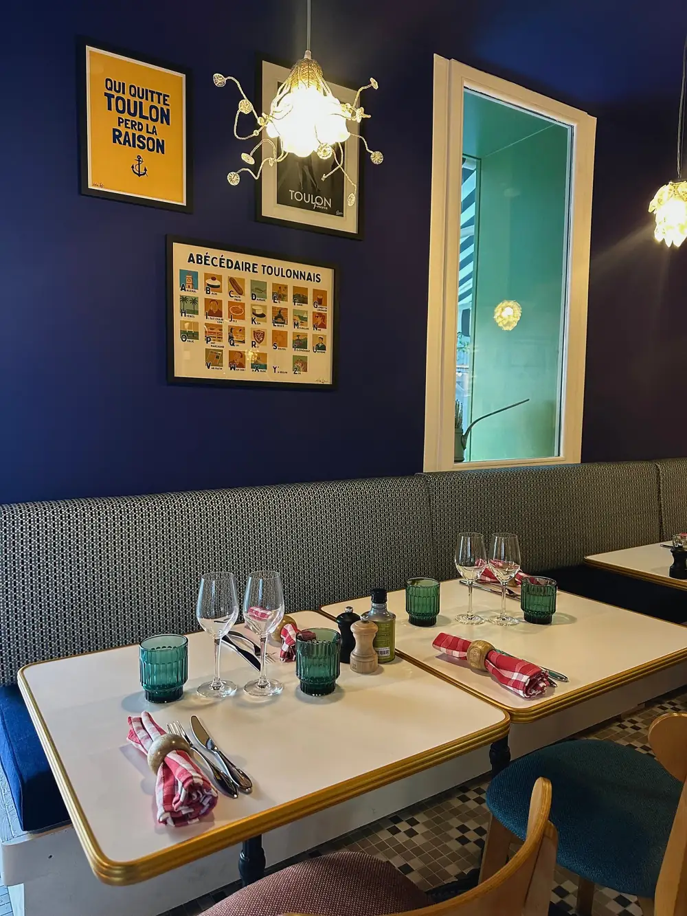 La salle côté mur bleu marine : banquette, tables au liseré jaune, verres turquoise et affiches sur Toulon